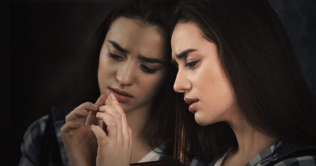 悩む表情の40代女性が鏡を見つめ、「私にはもう無理かも」と感じている様子。年齢や自信低下により自己効力感が下がりやすくなるイメージ